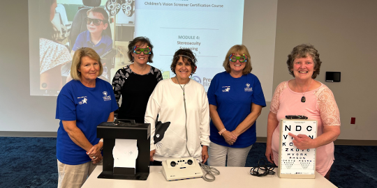 Five volunteers display hearing and vision screening equipment