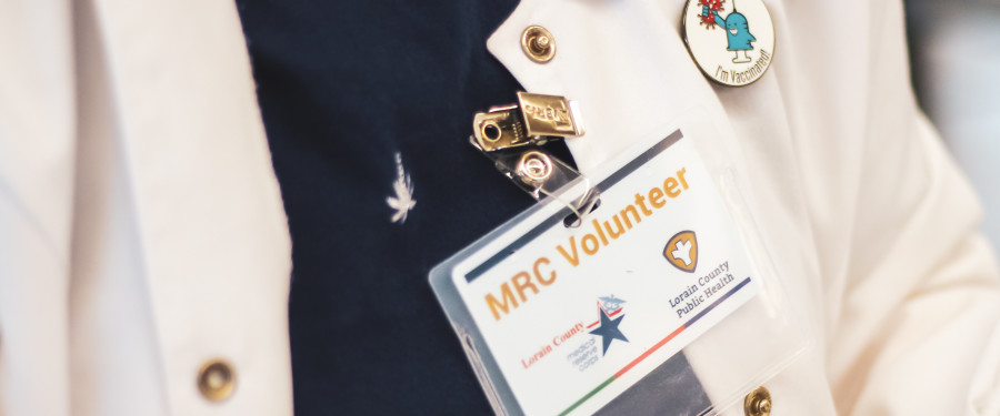 a badge of a Medical Reserve Corps (MRC) volunteer with a white coat and pin 