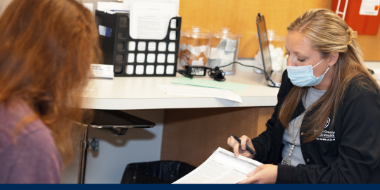 Lorain County Public Health nurse answers client questions holding a fact sheet wearing a black lab coat with the LCPH logo