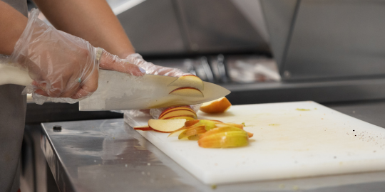 a person with gloves chops apple slices on a cutting board at a restaurant 