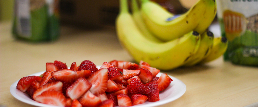 Cut strawberries sit on a plate and a bundle of bananas is next to them 